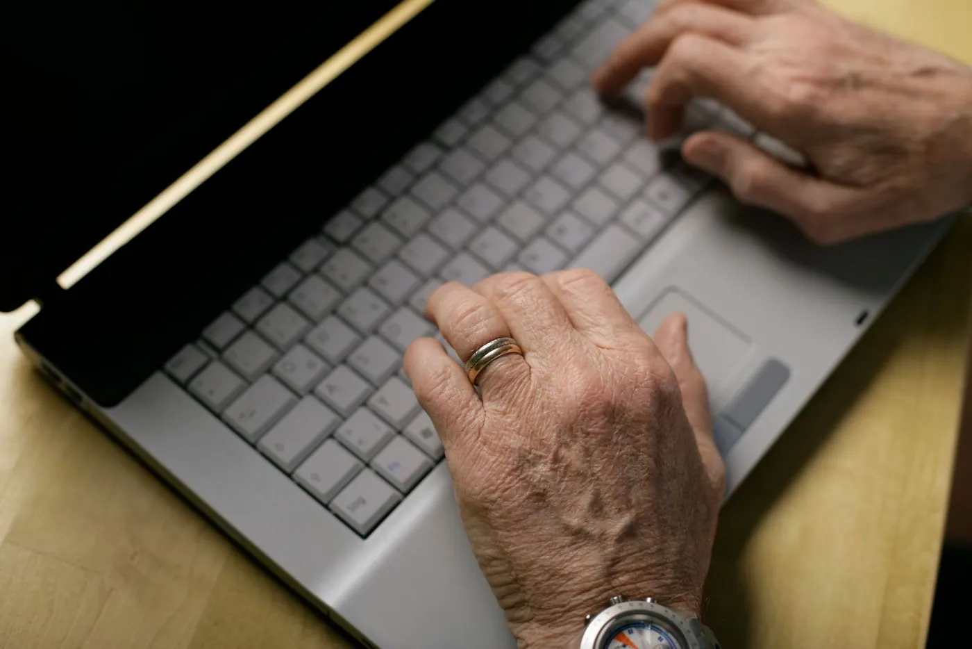 Hände einer älteren Person tippen auf einer Laptop-Tastatur